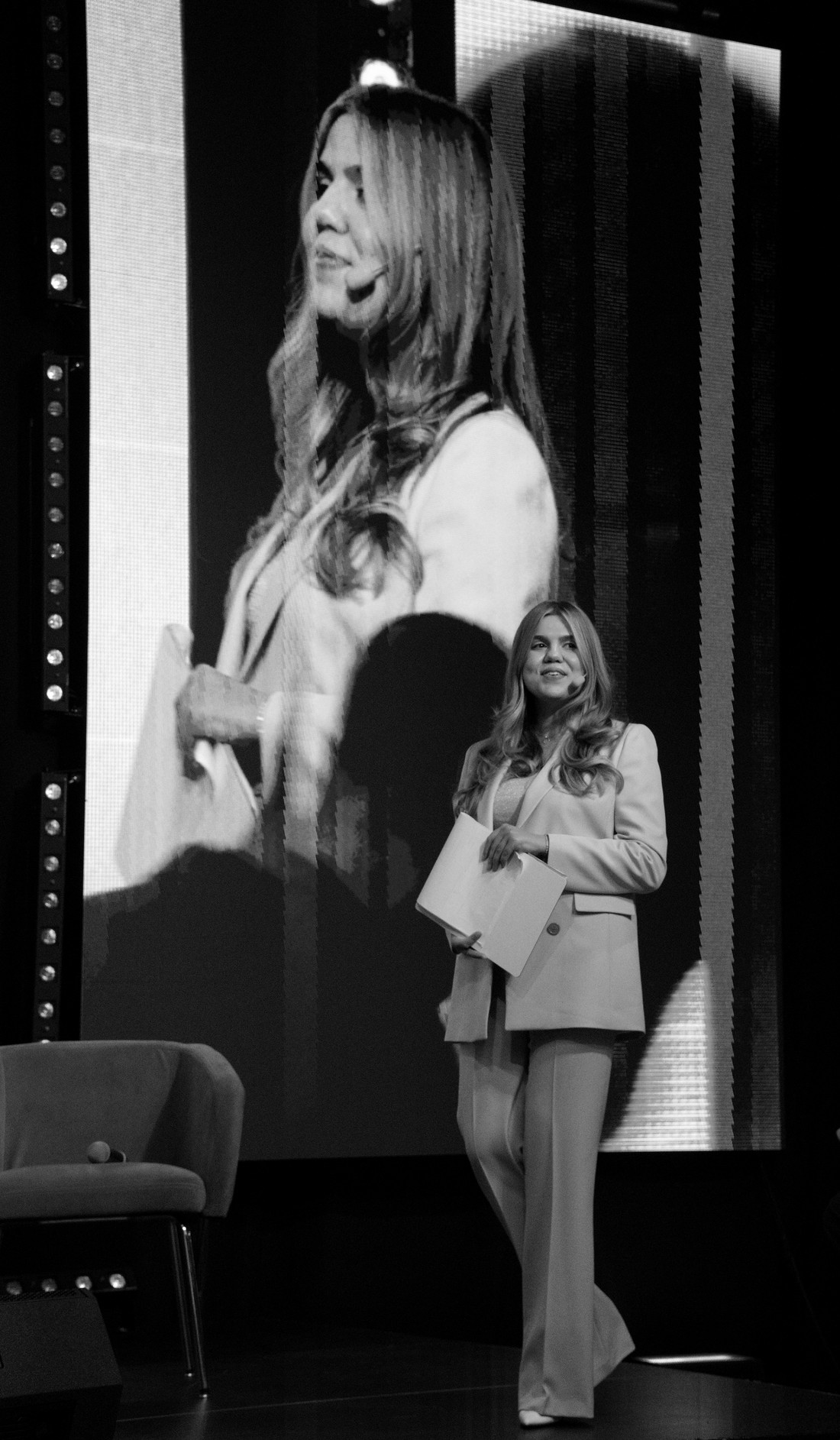 Cornelia Bicherschi speaking on stage with her image projected on a large screen behind her